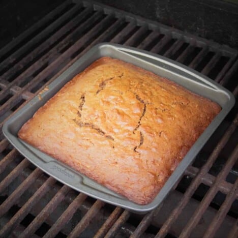 A square metal baking pan is in the oven with a golden brown carrot cake baking inside.