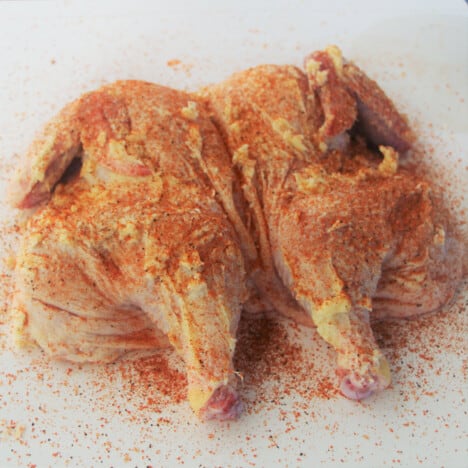 Looking at a flattened chicken with seasoned butter and coating of rub on it.