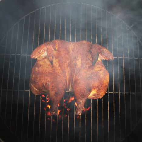 Looking down on a flattened chicken cooked over charcoal in a round BBQ.