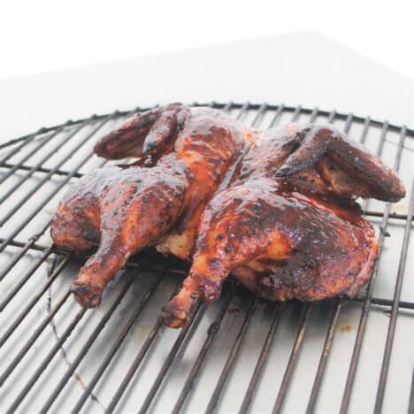 A cooked flattened chicken sitting on a grill rack.