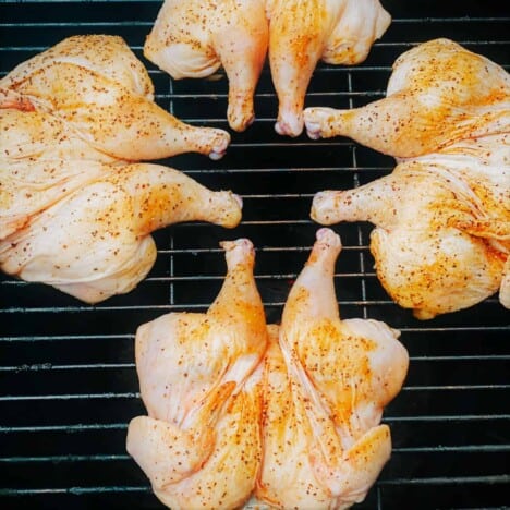 Four small chickens are butterflied and laid flat on a grill grated.