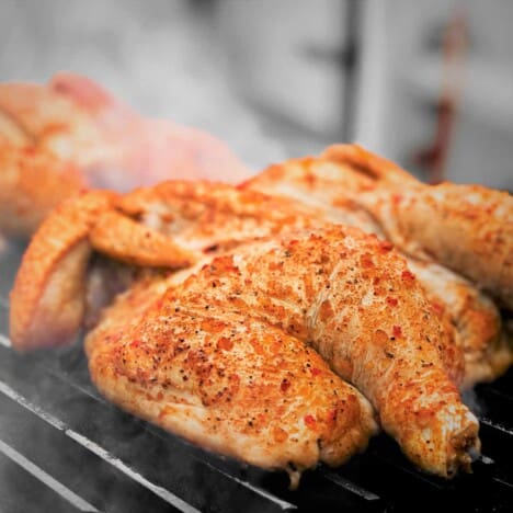 A seasoned, raw, butterflied chicken is cooking on a grill.