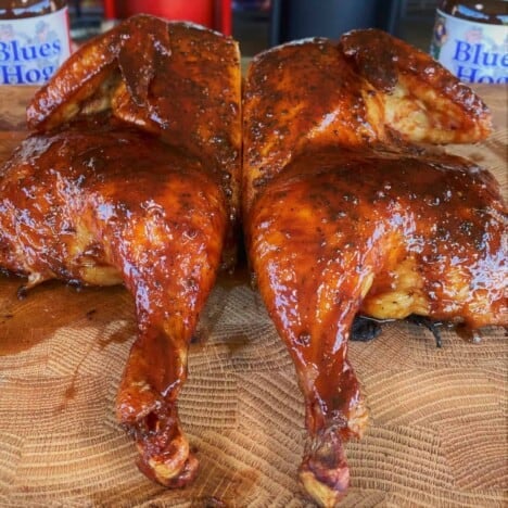 A cooked and glazed butterflied chicken rests on a wooden cutting board.