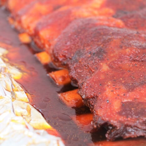 Close up look of cooked ribs on foil with their liquid showcasing the pullback on the bone.