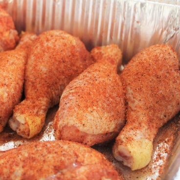 Rub-coated raw chicken drumsticks resting in a foil pan.