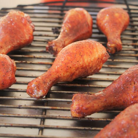 Glazed chicken drumsticks sitting on a round grill rack.