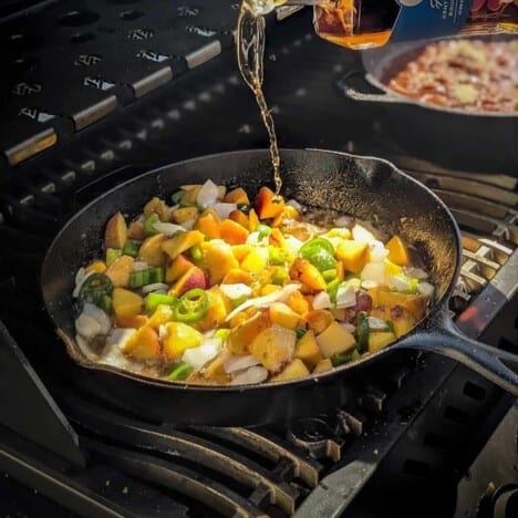 Chunks of peaches, bell peppers, and onions cook in a cast iron skillet on the grill.