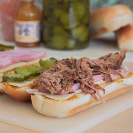 Looking down onto an open-faced pulled pork sandwich, with layers of pulled pork and pickles, with ingredients in the background.