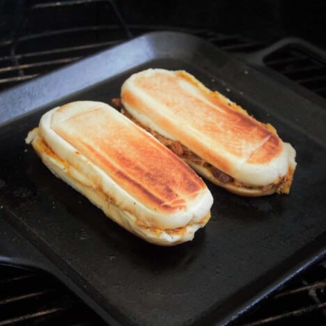 Two pulled pork Cuban sandwiches with golden brown crusts are on a flat skillet.