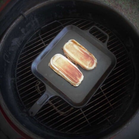 Tow pulled pork Cuban sandwiches are cooking on a flat top grill on top of a traditional grill.