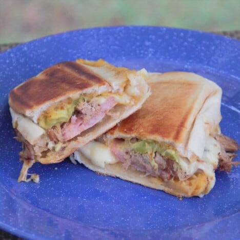 A pulled pork cuban sandwich is sliced in half and resting on a blue camping plate.