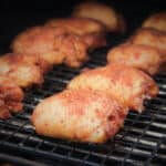 Seasoned raw chicken thighs are lined up on a grill.