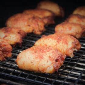 Seasoned raw chicken thighs are lined up on a grill.