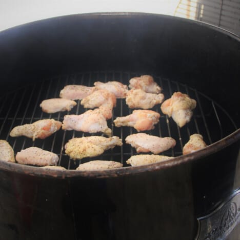 Raw chicken wings with a rub sitting in a round smoker.
