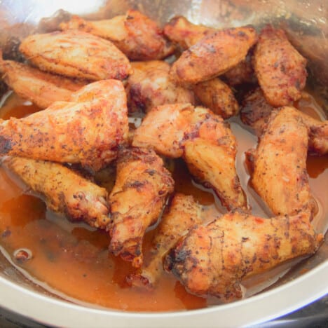 Chicken wings in a stainless bowl with the sriracha and honey sauce to coat them.