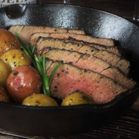 Grilled and sliced filet mignon rests in a cast iron skillet alongside butter roasted whole baby potatoes.