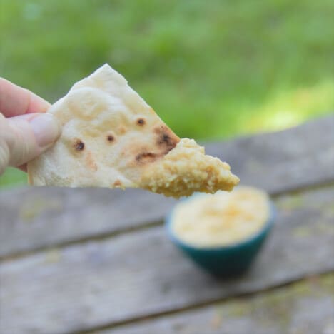 A pita chip having a dip of hummus on it.