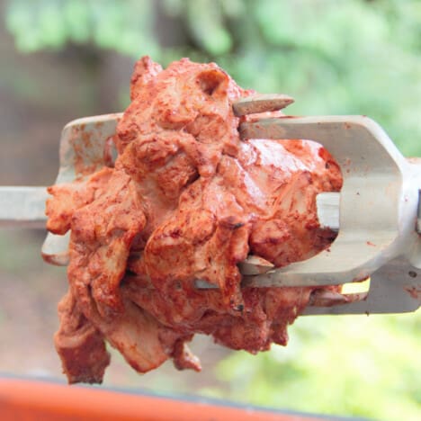 A spit with two clamps holding raw tandoori marinated chicken in place.