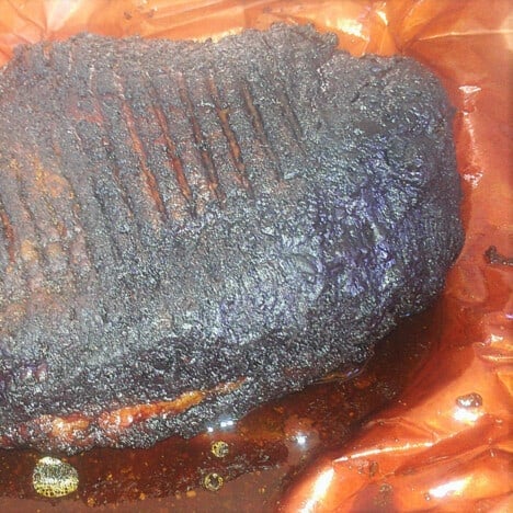 A fully cooked brisket having been unwrapped but still sitting on the pink paper.