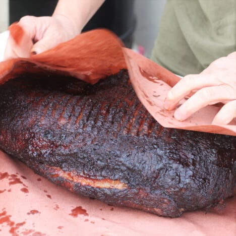 A partually cooked brisket is being wrapped in pink butcher's paper.