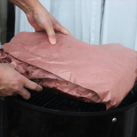 A brisket wrapped in pink paper is being place into a smoker.