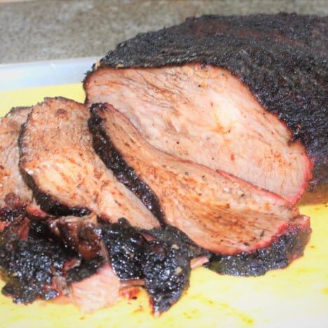 A piece of brisket with with a dark bark partly sliced.