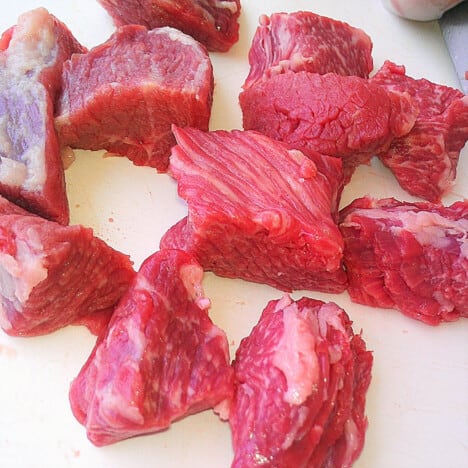 Dice chuncks of beef all the same size sitting on a white chopping board.