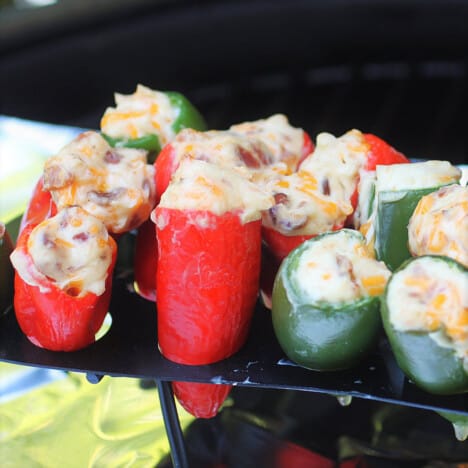 Red and green whole stuffed jalapeno peppers sitting in a rach in a barbecue.