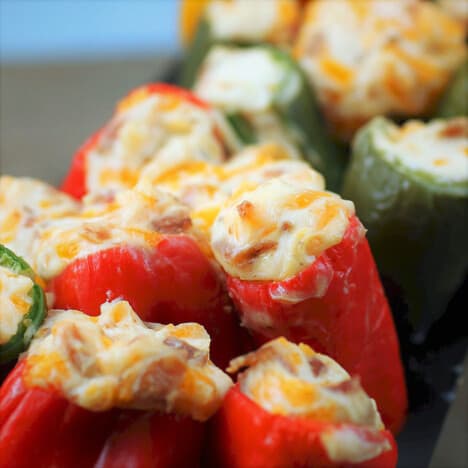 Close up of red and green cheesy jalapeno poppers sitting upright being cooked.