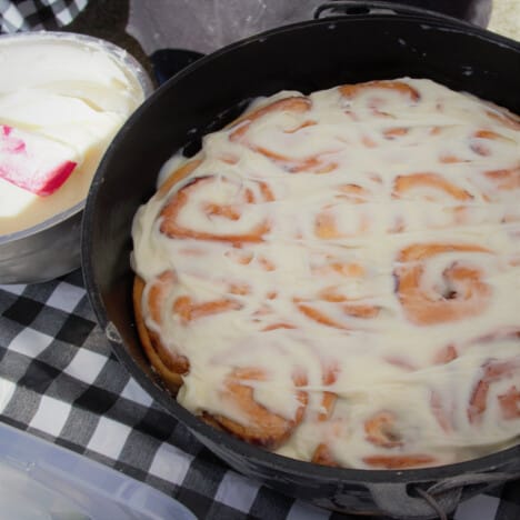 A Dutch oven with frosted sweet rolls with the bowl of frosting sitting next to it.