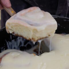 A frosted five spice sweet roll being removed from a Dutch oven.