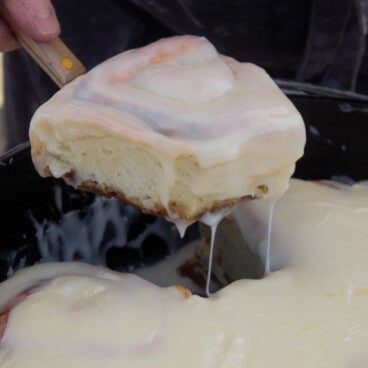 A frosted five spice sweet roll being removed from a Dutch oven.
