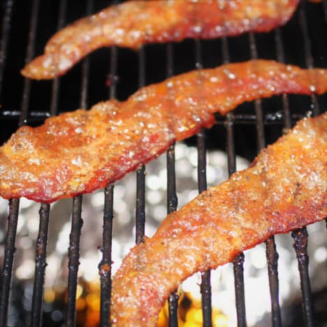 Three pieces of bacon pig candy cooking on a grill rack.