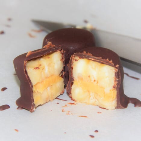 Banana slices make a peanut butter sandwich coated in chocolate cut in half to see the layers.