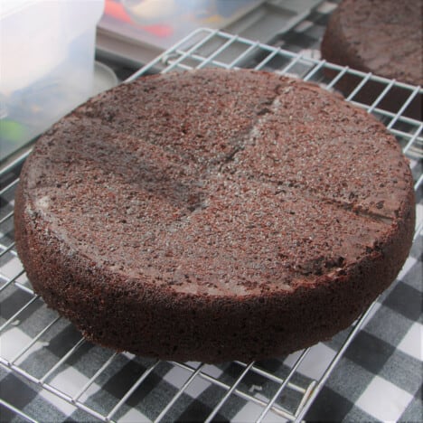 A chocolate cake placed upside down on a cooling rack.