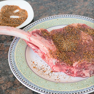 A raw tomahawk steak on a plate sprinkled with rub.