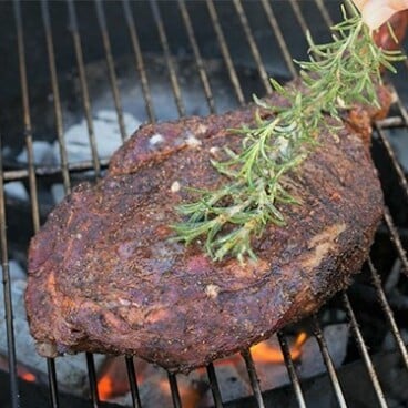 A sprig of rosemary brushing a grilled tomahawk steak on a grill grate.