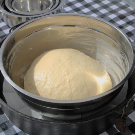 A ball of dough in a stainless bowl rising.