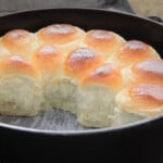 A batch of bread rolls still sitting in the Dutch oven on parchment paper with some aready removed and served.