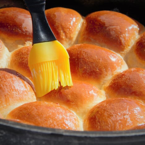 The brown tops of cooked bread rolls being brished with butter.