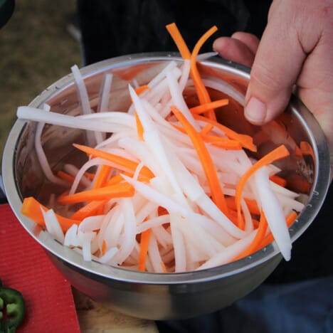 A stainless bowl filled with thinly cut carrots and daikon radish.