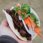 A pulled brisket taco topped with vegetables being held.
