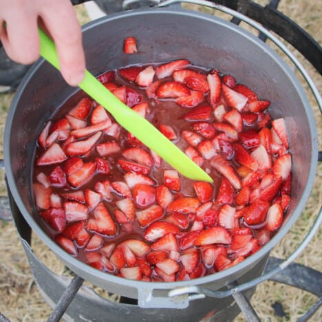 Fresh strawberry pieces simmering in a Dutch oven over a camp stove.