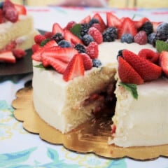 A served cake with a cut missing showing the strawberry compote withing and decrotive fresh strawberries on top.