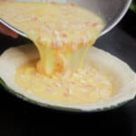 A runny bacon and egg filling is being poured into a prepared pie shell in a camp plate.