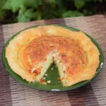 Green enamel camp plate with an egg and bacon pie in it with a single slice cut out and removed.