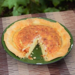 Green enamel camp plate with an egg and bacon pie in it with a single slice cut out and removed.