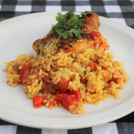 A white plate with a serving of yellow rice and tomato, topped with chicken.