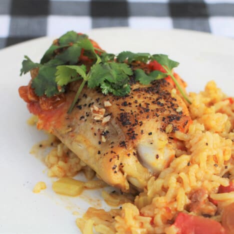 Close up of a chicken thigh served with curried rice and garnished with parsley.