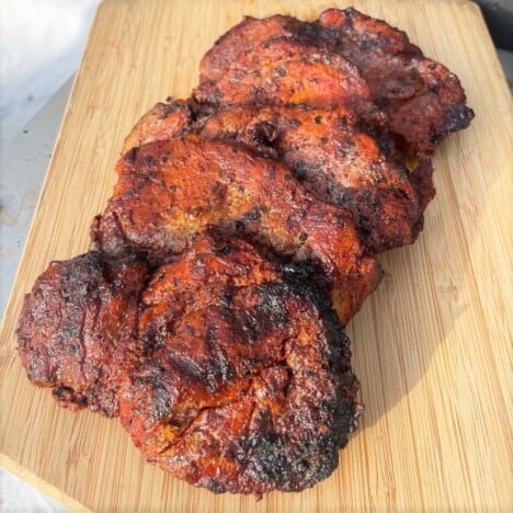 Pork steaks cooked to a rich mahogany color sitting on a chopping board.